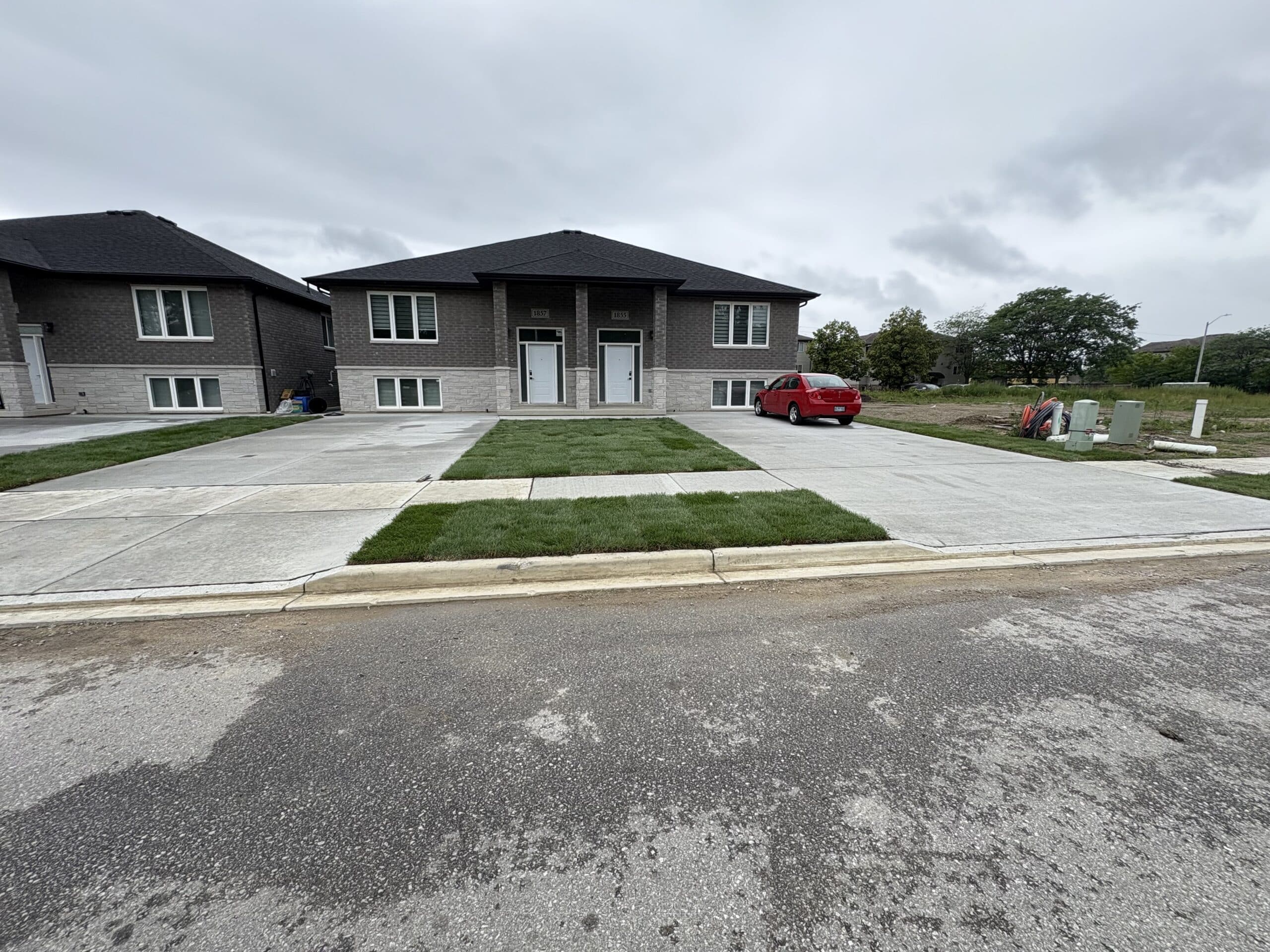 A duplex with a shared driveway, new grass sod, and a red car parked on the right side, under a cloudy sky.
